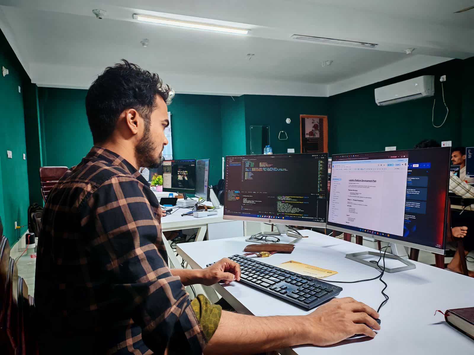 A developer building a website on a dual-monitor setup with code and a project plan on screen